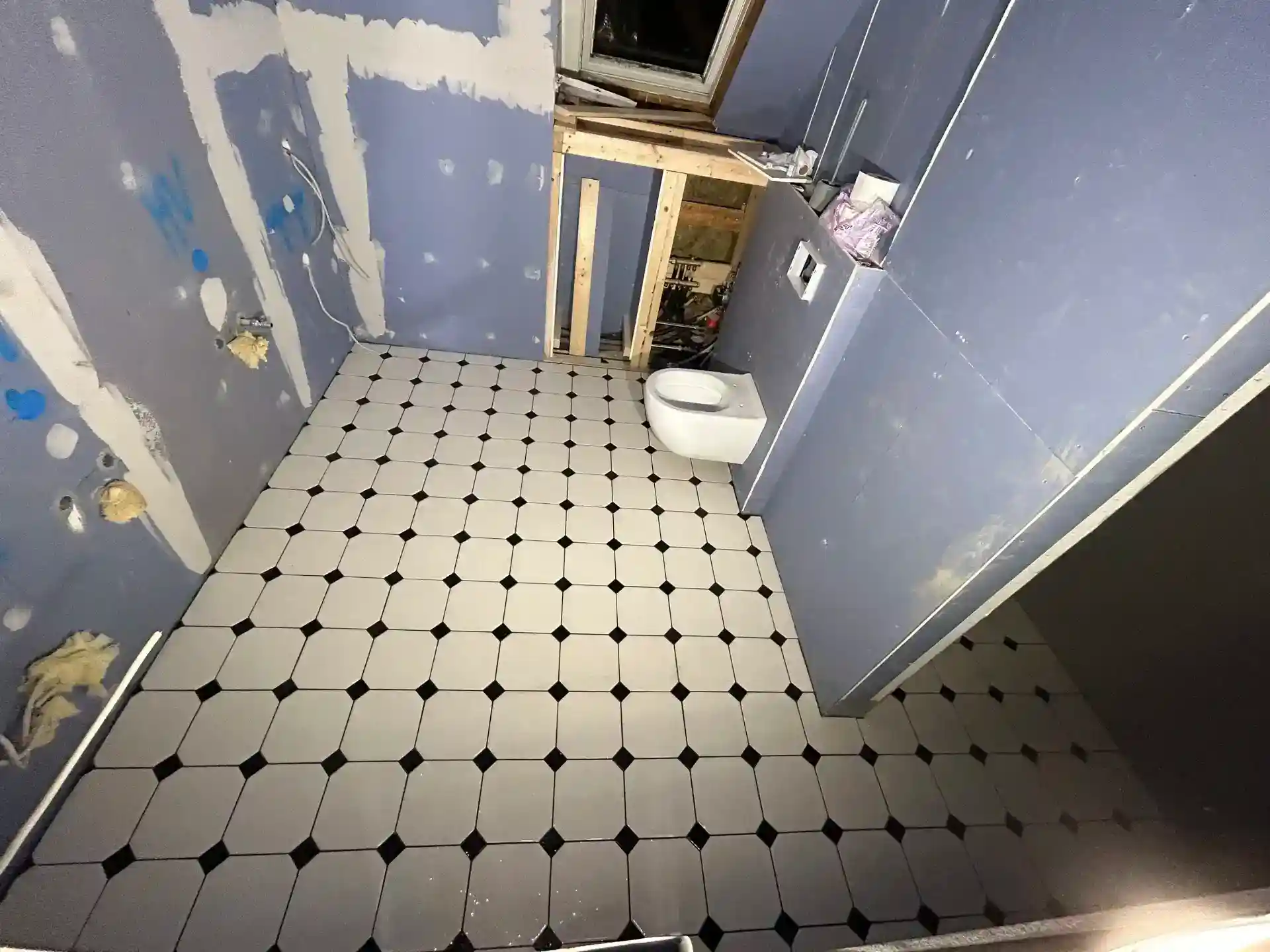 Køkken- eller badeværelses-værelse under renovering med nye hvide fliser og installationsarbejde.