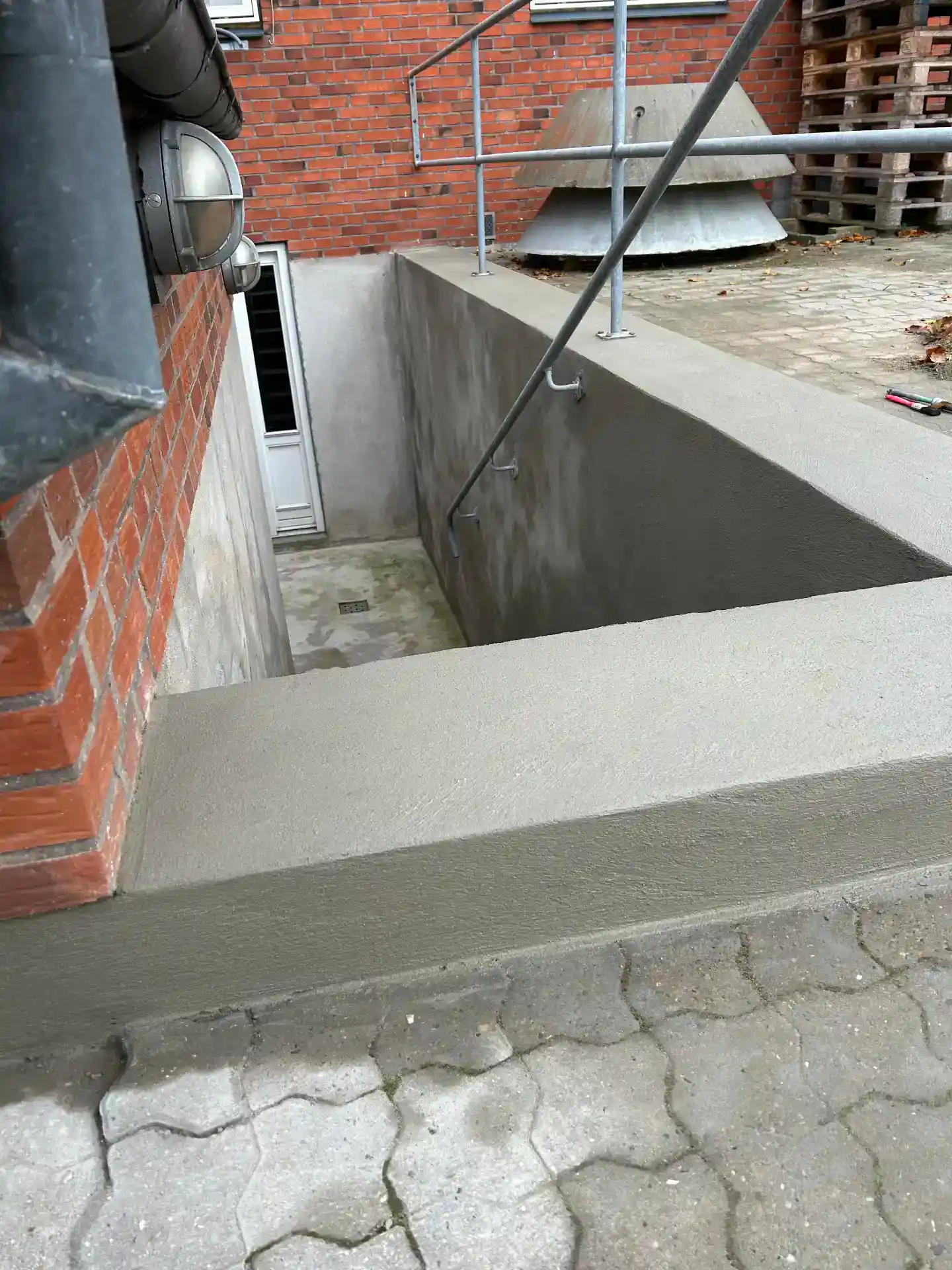 Beton-renovering under trappe til kælder med sikkerhedsgelænder.